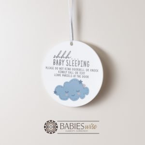 Round white acrylic plaque with hole for hanging on a door, UV printed with "shhh... baby sleeping with message and a blue sleeping cloud illustration. Styled hanging by a ribbon.