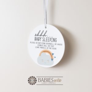 Round white acrylic plaque with hole for hanging on a door, UV printed with "shhh... baby sleeping with message and a cloud and rainbow illustration. Styled hanging by a ribbon.