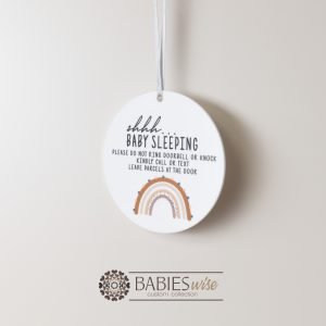 Round white acrylic plaque with hole for hanging on a door, UV printed with "shhh... baby sleeping with message and a brown toned rainbow. Styled hanging by a ribbon.