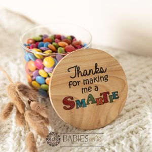 Glass gift jar timber lid featuring UV printed quote "Thanks for making me a smarty" filled with colourful chocolates. Styled with a soft blanket.