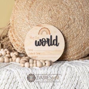 Round timber "Hello World" birth announcement plaque UV printed rainbow and raised 3D acrylic "Hello" featuring spaces for baby's name, date of birth, weight and length. Styled wit a soft blanket and woven pillow.