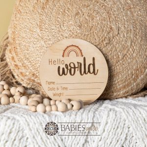 Round timber "Hello World" birth announcement plaque with UV printed rainbow and printed spaces for baby's name, date, time, weight and lenght. Styled on a soft white blanket with a woven pillow & wooden beads.