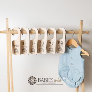 Timber wardrobe divider hangers with blue rainbow design, labelled newborn to 24 months. Styled with divider hangers with baby clothes.