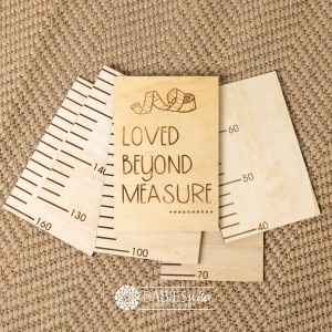 Timber growth chart with five panels and laser engraved header with "Loved beyond Measure" text with a tape measure design. Styled with a woven mat.