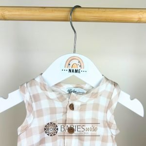 White personlised children's hanger with brown- tone rainbow and custom name. Styles on a hanger with baby's clothes.