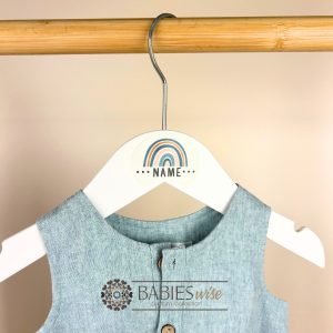 White personlised children's hanger with bblue- tone rainbow and custom name. Styles on a hanger with baby's clothes.