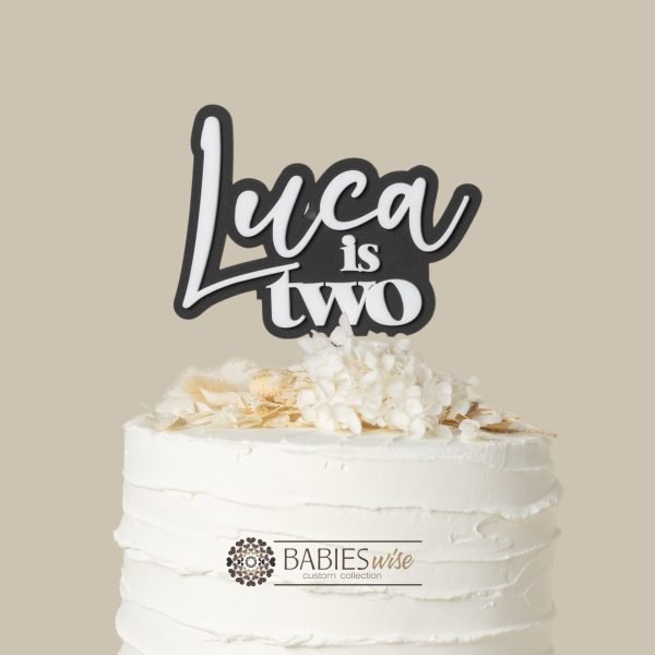Personlised "is two" acrylic cake topper with a child's name in layered 3D design. Styled with a cake and flowers.