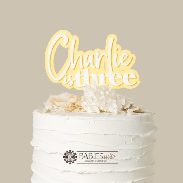 Personlised "is three" acrylic cake topper with child's name in layered 3D design. Styled with cake and flowers.