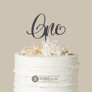 "One" script cake topper in a range of materials to display on a birthday cake for a first birthday celebration. Styled on a cake with flowers.
