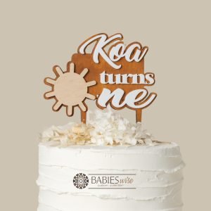 Personlised first birthday cake topper featuring a timber sun design, a custom name, and raised 3D acrylic lettering reading "turns one". Styled on a white cake with flowers.