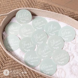 Baby monthly milestone discs in soft mint UV printed acrylic discs with white cursive script lettering with a motif leaf. Styled on a woven bassinett on a woven neutral mat.