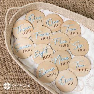 Baby milestone discs with natural timber base and raised baby blue 3D acrylic flowing cursive script months with printed week, months and year. Styled on a woven bassinett on a woven neutral mat.