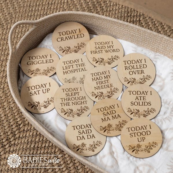 "Today I" Baby milestone plaques laser engraved on timber discs with a floral design. Styled on a woven bassinett on a woven neutral mat.