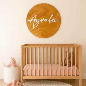 Personlised Stained circular timber nursery name sign with raised 3D scrylic script lettering. Styled above a wooden cot in neutral nursery.