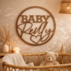 Round laser cut timber hoop sign with bold uppercase lettering word "BABY" and in a flowing cursive lettering surname with a love heart beneath. Styled in a nursery theme.