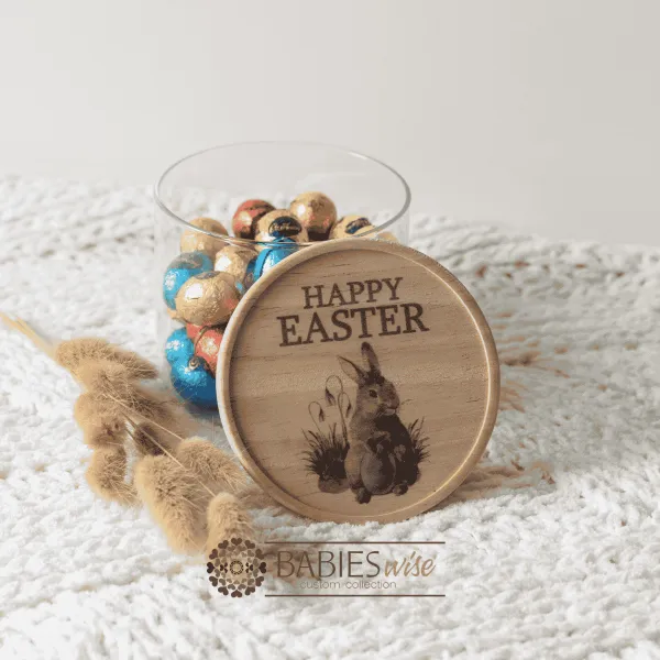 Glass Easter jar with a UV printed timber lid in a Happy Easter with a bunny design. Styled on a soft blanket with the jar filled with Easter eggs.