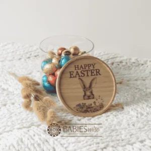 Glass Easter jar with a UV printed timber lid in a Happy Easter with a bunny design. Styled on a soft blanket with the jar filled with Easter eggs.