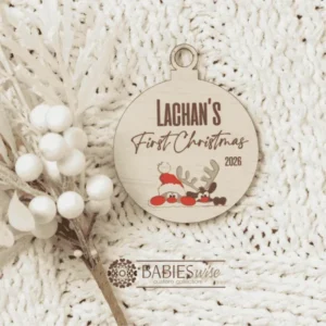 Round timber Christmas bauble UV printed with a selection of designs to choose from and personlised child's name and "First Christmas" with the year. Includes a hole to hang from the Christmas Tree. Style on a warm, soft blanket with a white Christmas wreath.