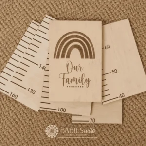Laser engraved timber growth chart featuring a rainbow design with the words "our Family" in script font, displayed with timber measuring panels. Styled on a woven mat.