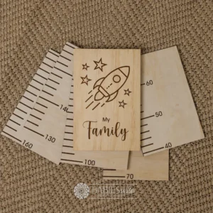 Laser engraved timber growth chart header featuring a rocket flying through stars above the words "My Family" in script lettering. Styled on a woven mat.