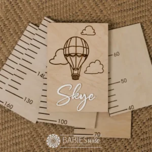 Personlised Timber Growth Charts laser engraved Header with a Hot Air Balloon and clouds with 3D acrylic child's name in script lettering. Styled as a flat-lay photo on a woven mat with the panels.