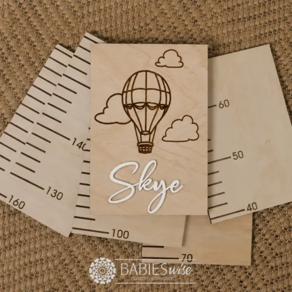 Personlised Timber Growth Charts laser engraved Header with a Hot Air Balloon and clouds with 3D acrylic child's name in script lettering. Styled as a flat-lay photo on a woven mat with the panels.