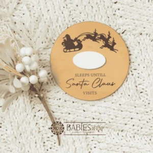 Round timber Christmas countdown plaque with a reusable white acrylic panel for writing the number of sleeps until Santa Claus visits. Available in two festive designs. Styled on a soft, white blanket.