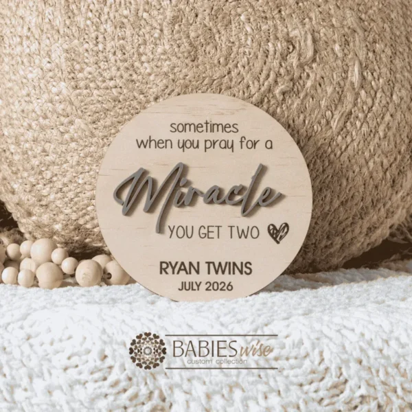 Round timber twin pregnancy announcement plaque featuring the phrase :sometimes when you pray for a Miracle, you get two" with the word "Miracle" in raised 3D acrylic . Personlised with the surname, month and year UV printed along the bottom of the plaque. Styled on a soft white blanket with a woven pillow & wooden beads.